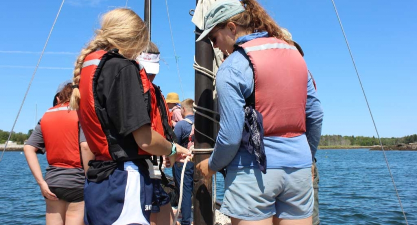 A group of students wearing life jackets work with ropes on a sailboat